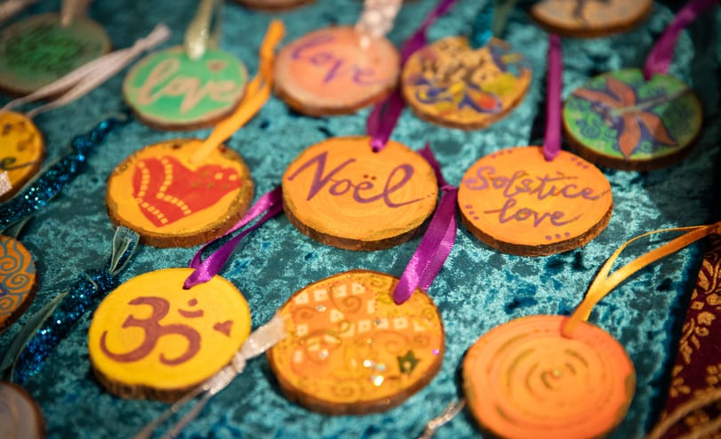 Hand-painted wooden Christmas decorations on ribbons, laid out on teal velvet, one reading “Noël” and another “Solstice love”.