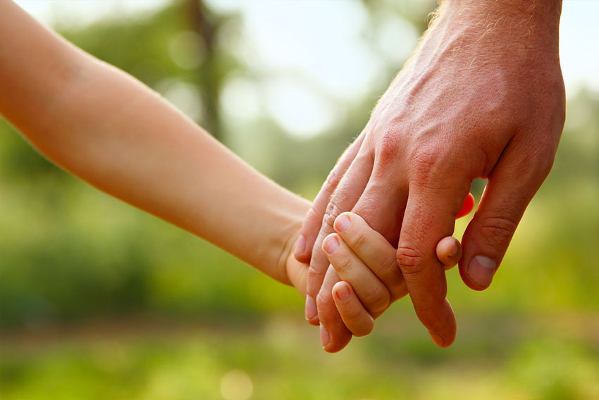 A close up image of a father and daughter holding hands in a beautiful green field.