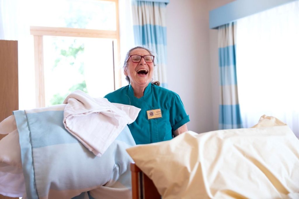 A laughing housekeeping volunteer organising bedsheets in Skanda Vale Hospice.